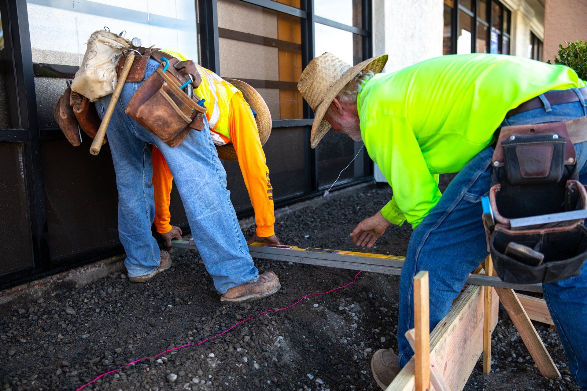 Two construction workers are working on a sidewalk in front of a building