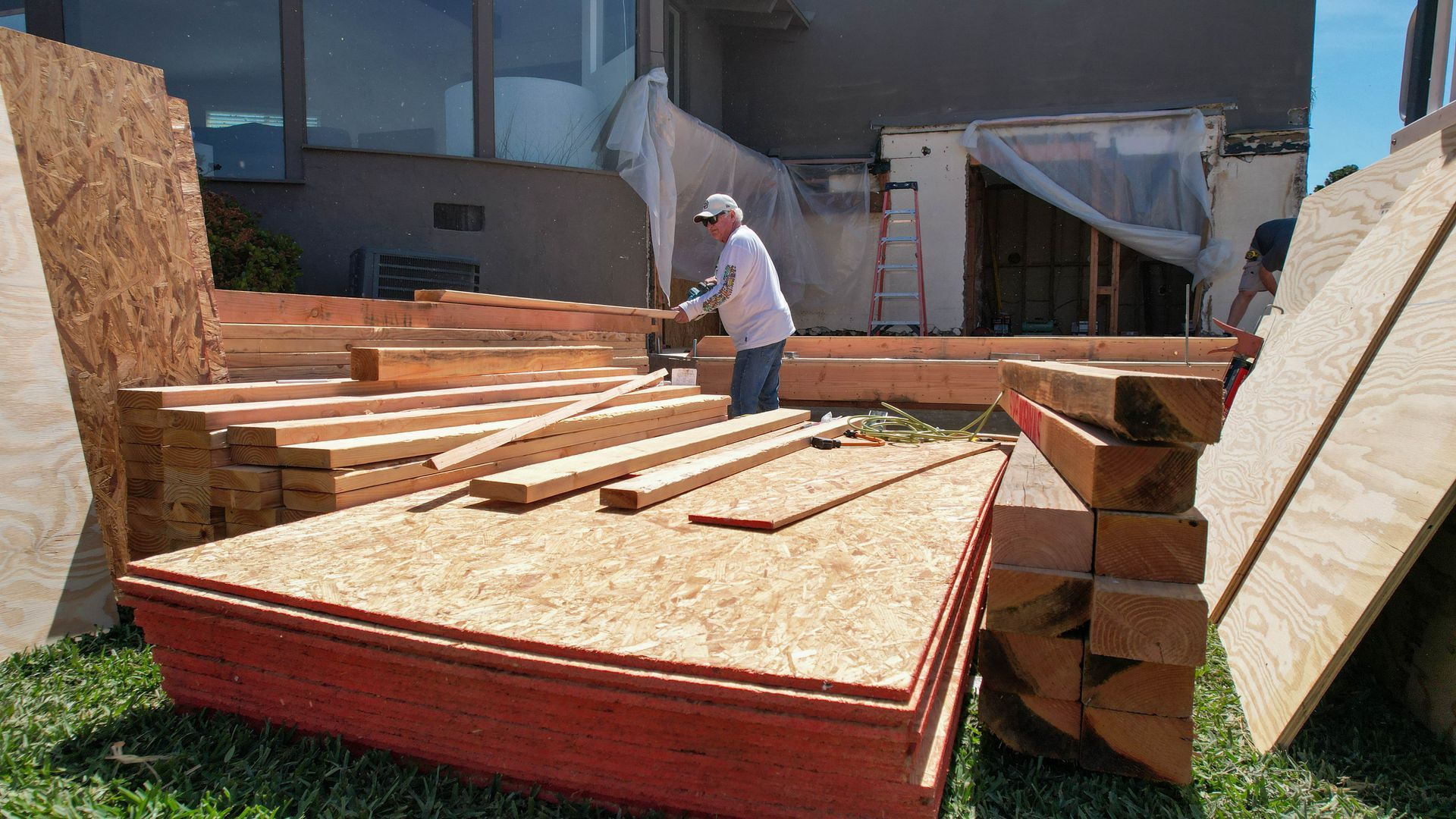 A man is working on a pile of wood in a yard.