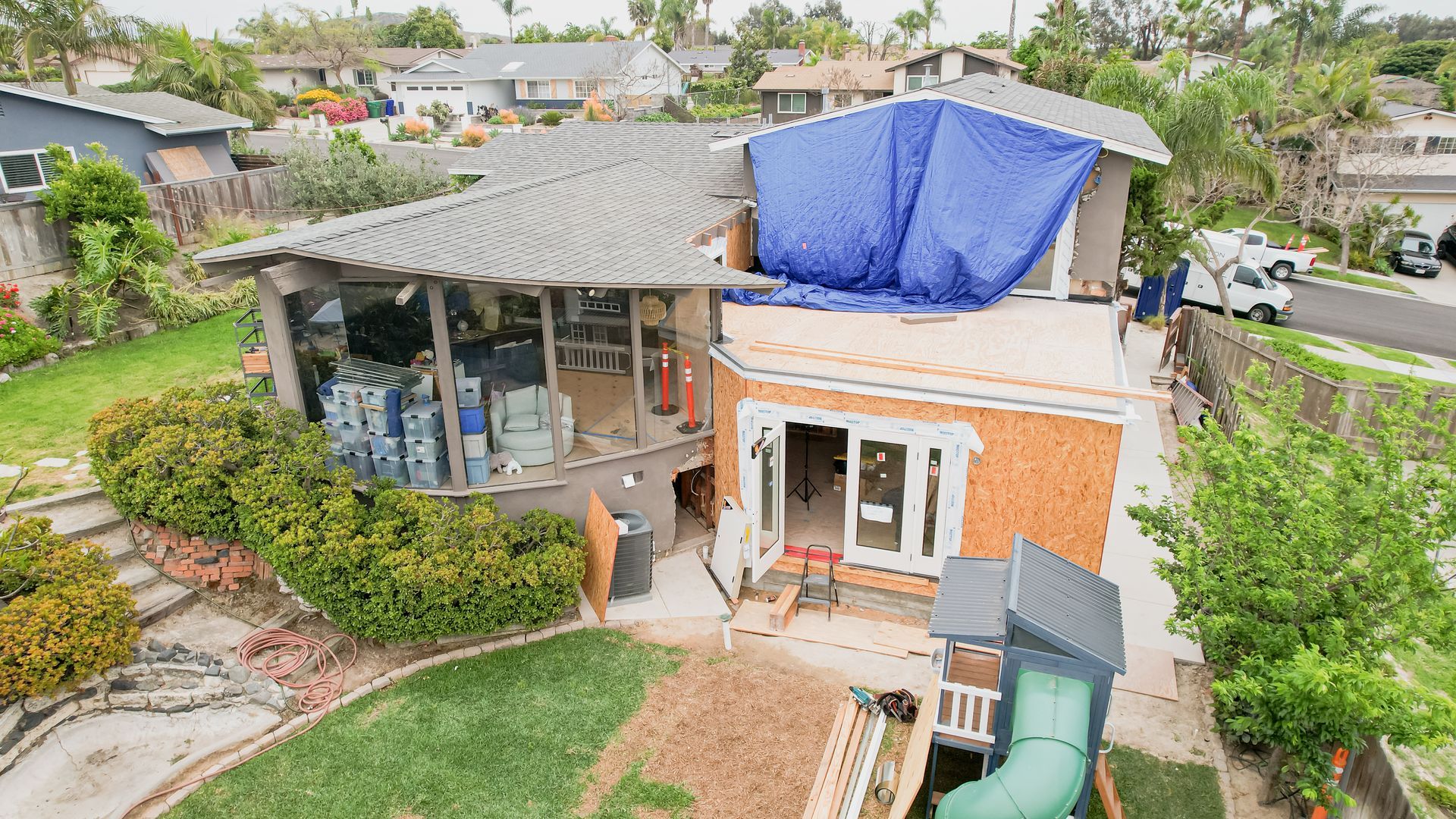 An aerial view of a house under construction with a blue tarp on the roof.