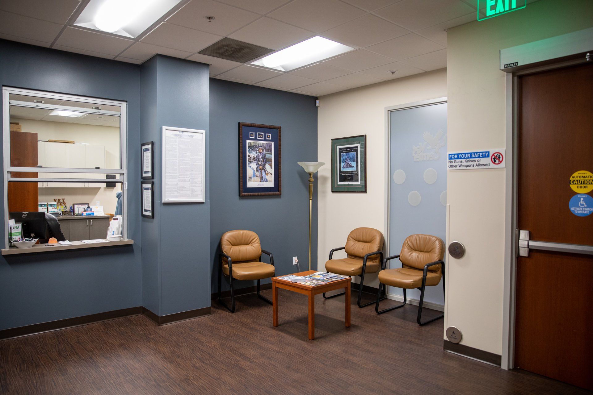 A waiting room with chairs , a table and an exit sign.