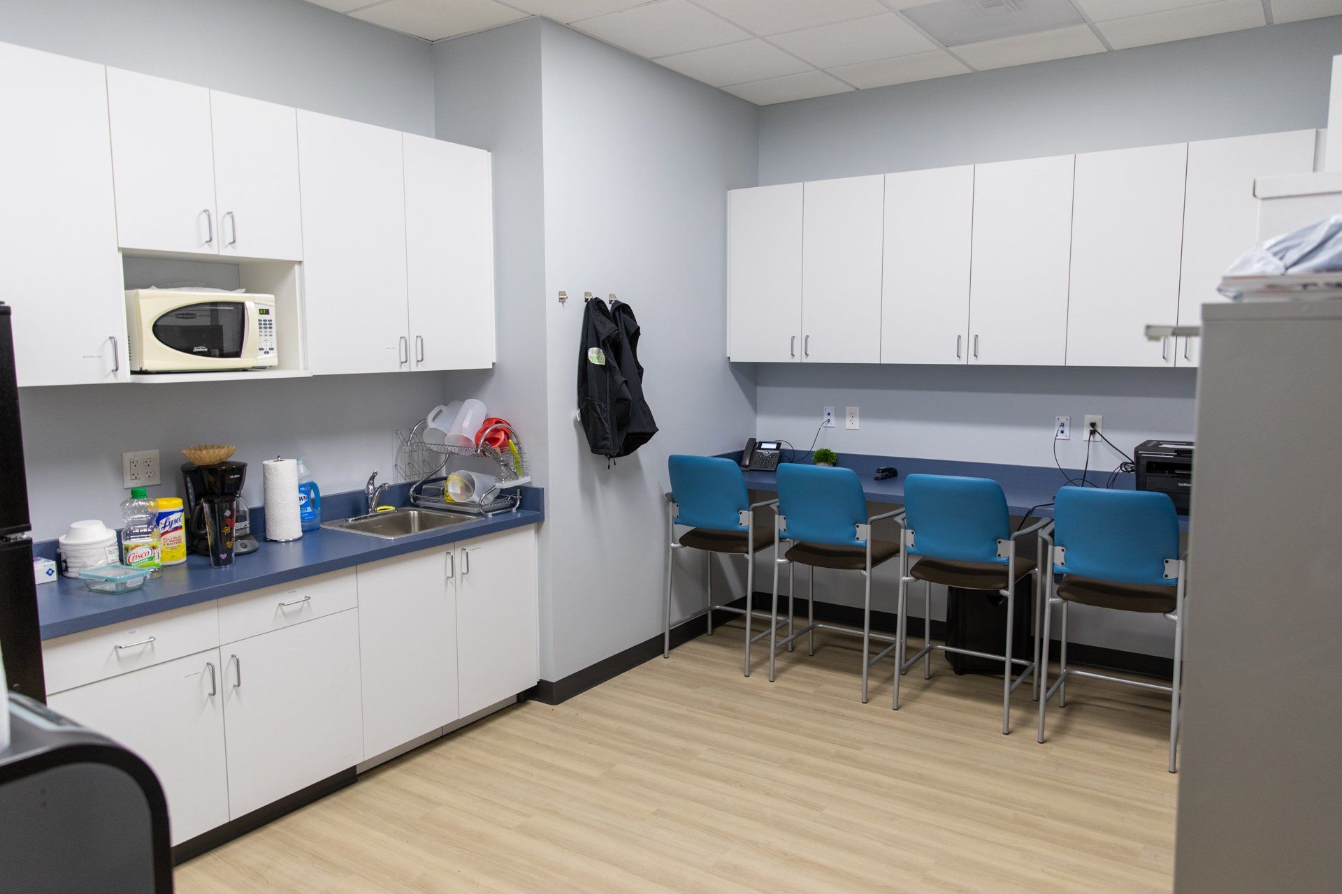 A kitchen with white cabinets , blue chairs and a microwave.