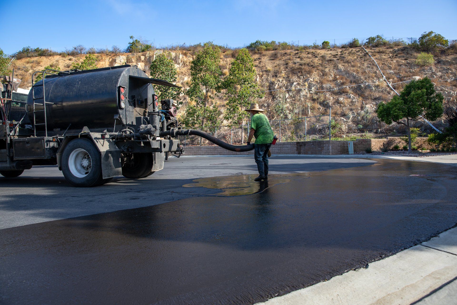 A man is pumping asphalt from a truck into a parking lot.