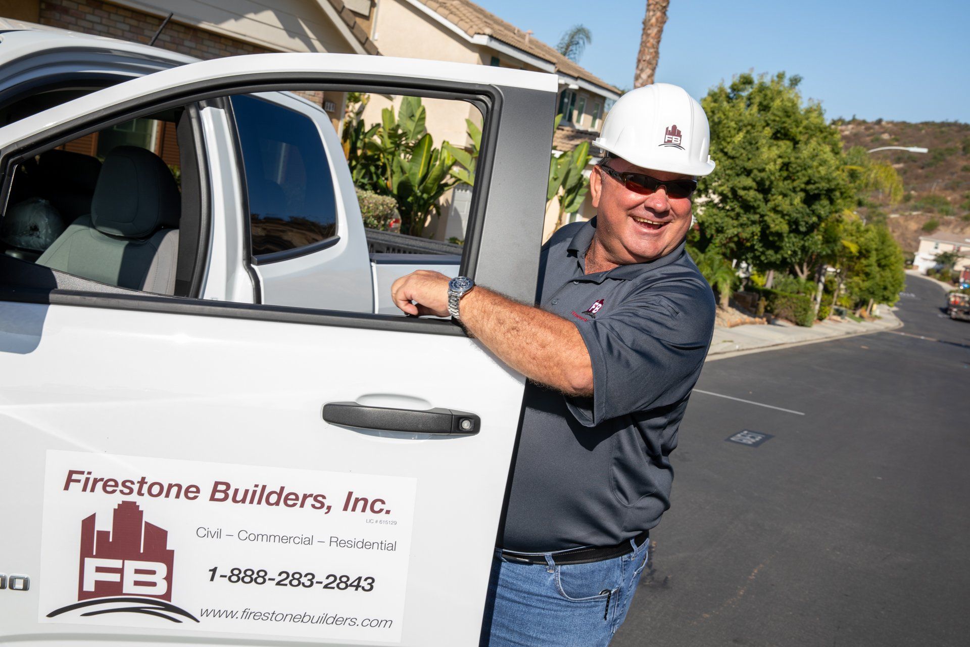 A man wearing a hard hat is standing next to a white truck.