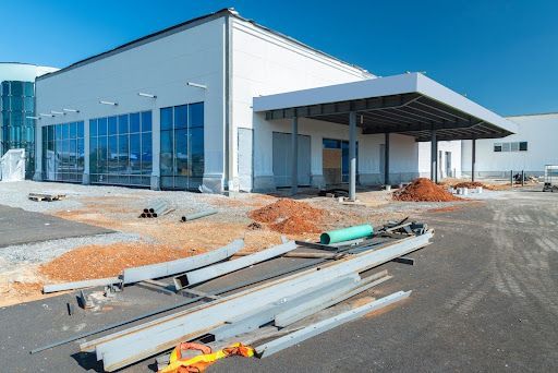 A newly constructed commercial building with large windows and a covered entrance, surrounded by construction materials.