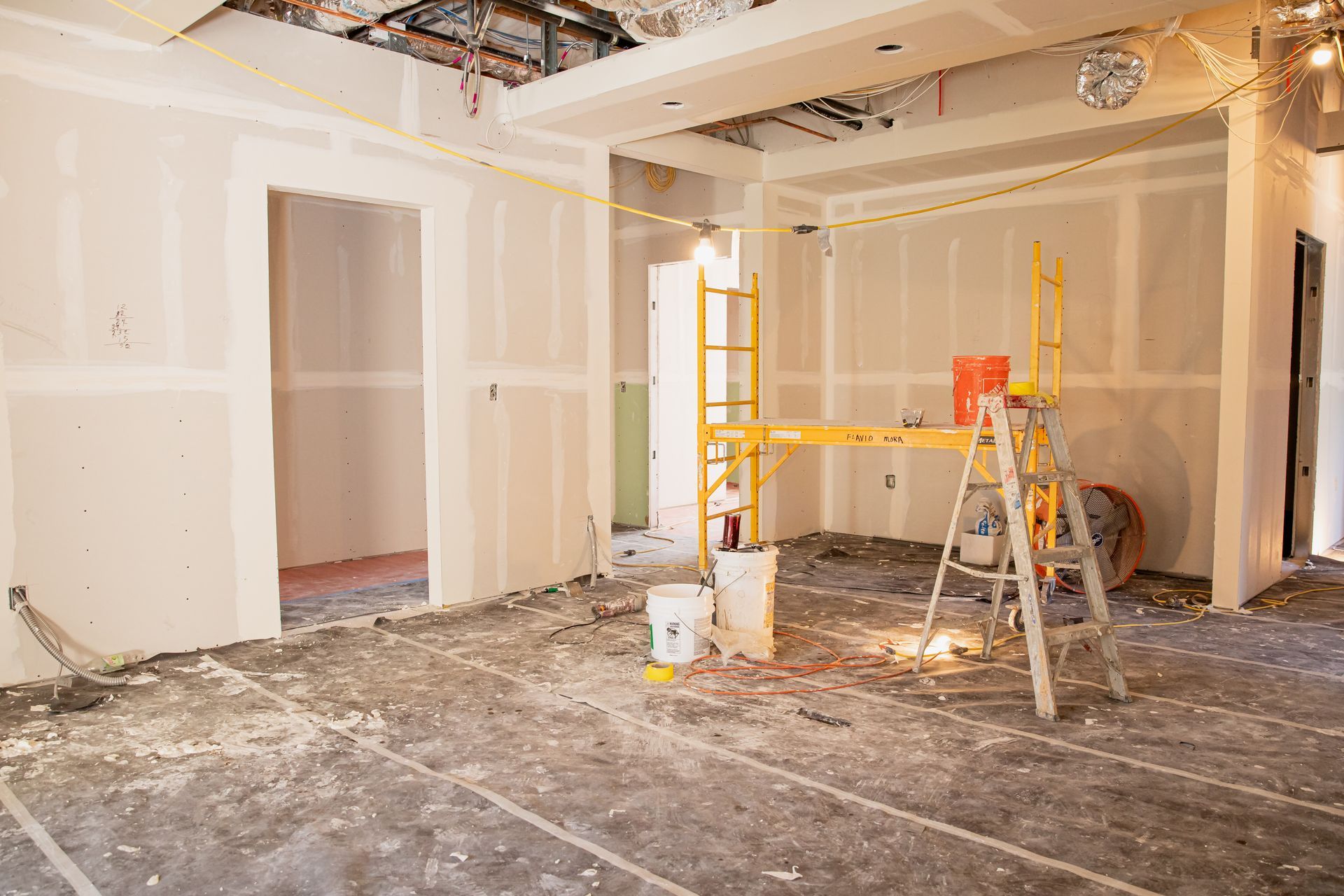 A room under construction with a ladder and buckets on the floor.
