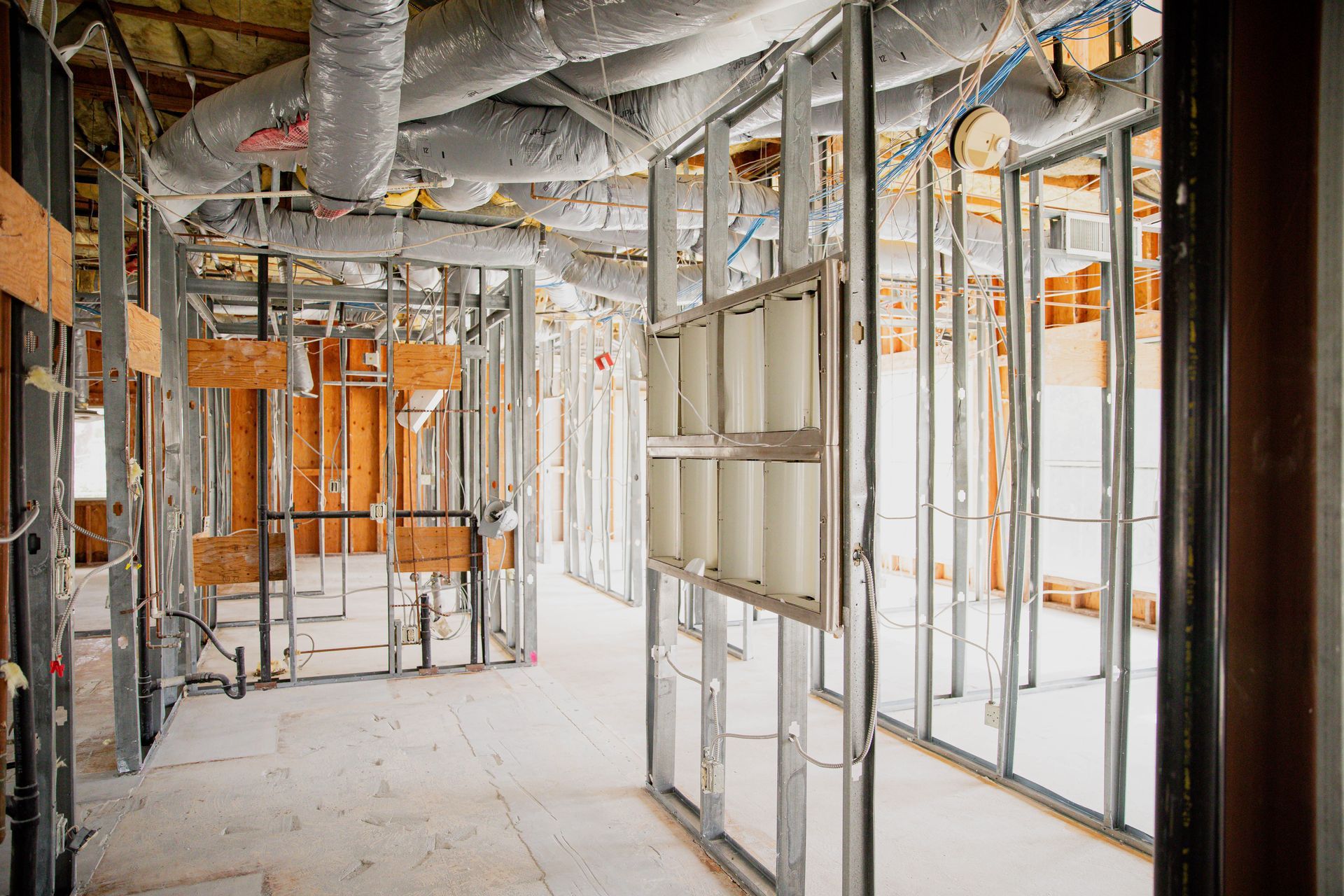 A hallway in a building under construction with a lot of pipes hanging from the ceiling.