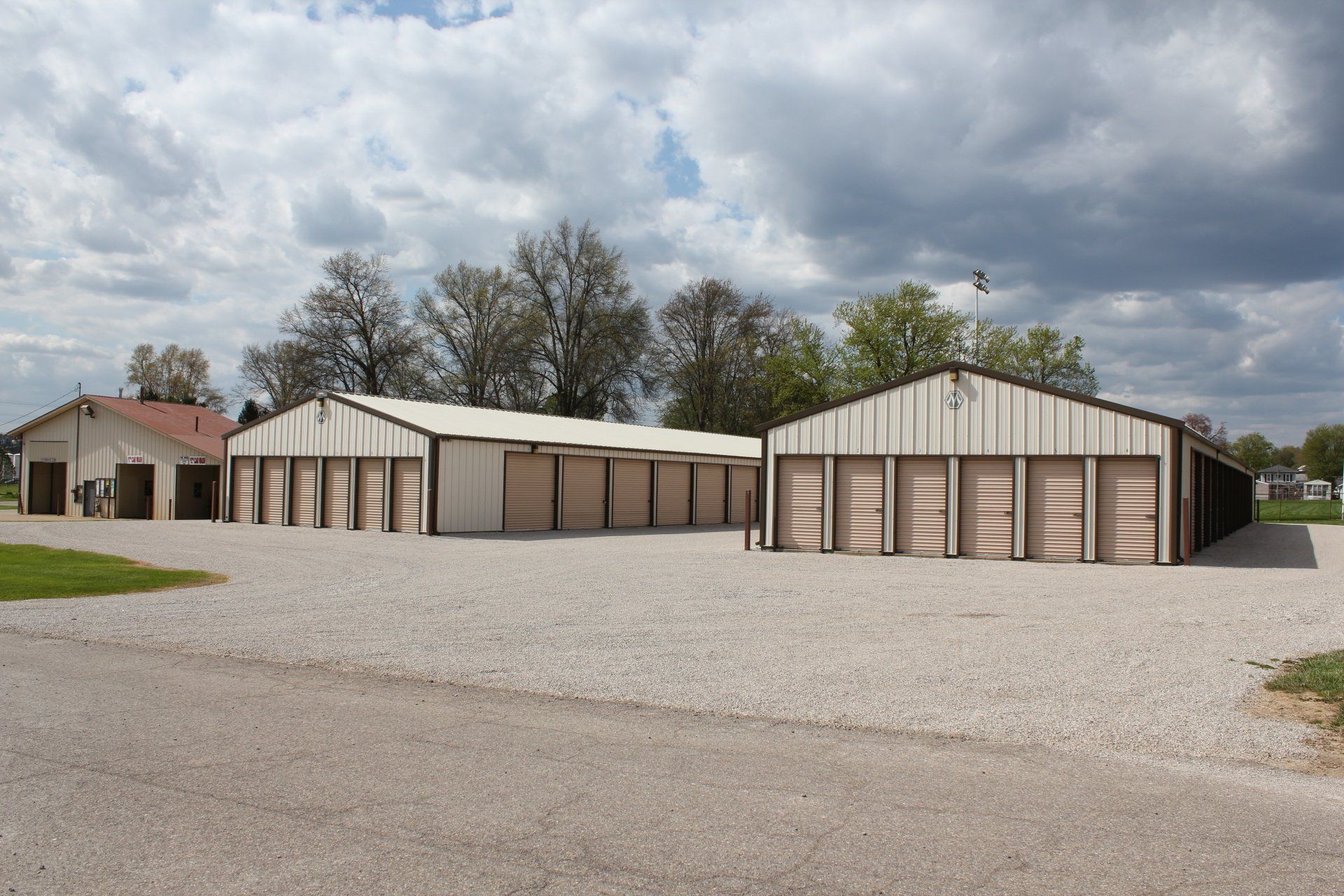 Storage units, several white metal buildings with brown doors, gravel lot, cloudy sky.