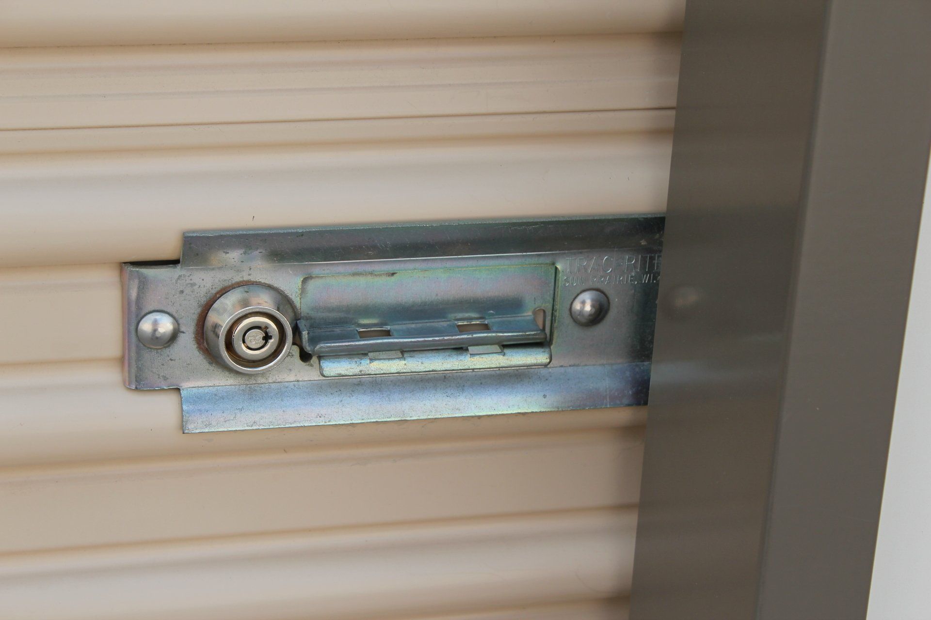 Metal lock on a tan roll-up door, with a gray metal frame visible to the right.
