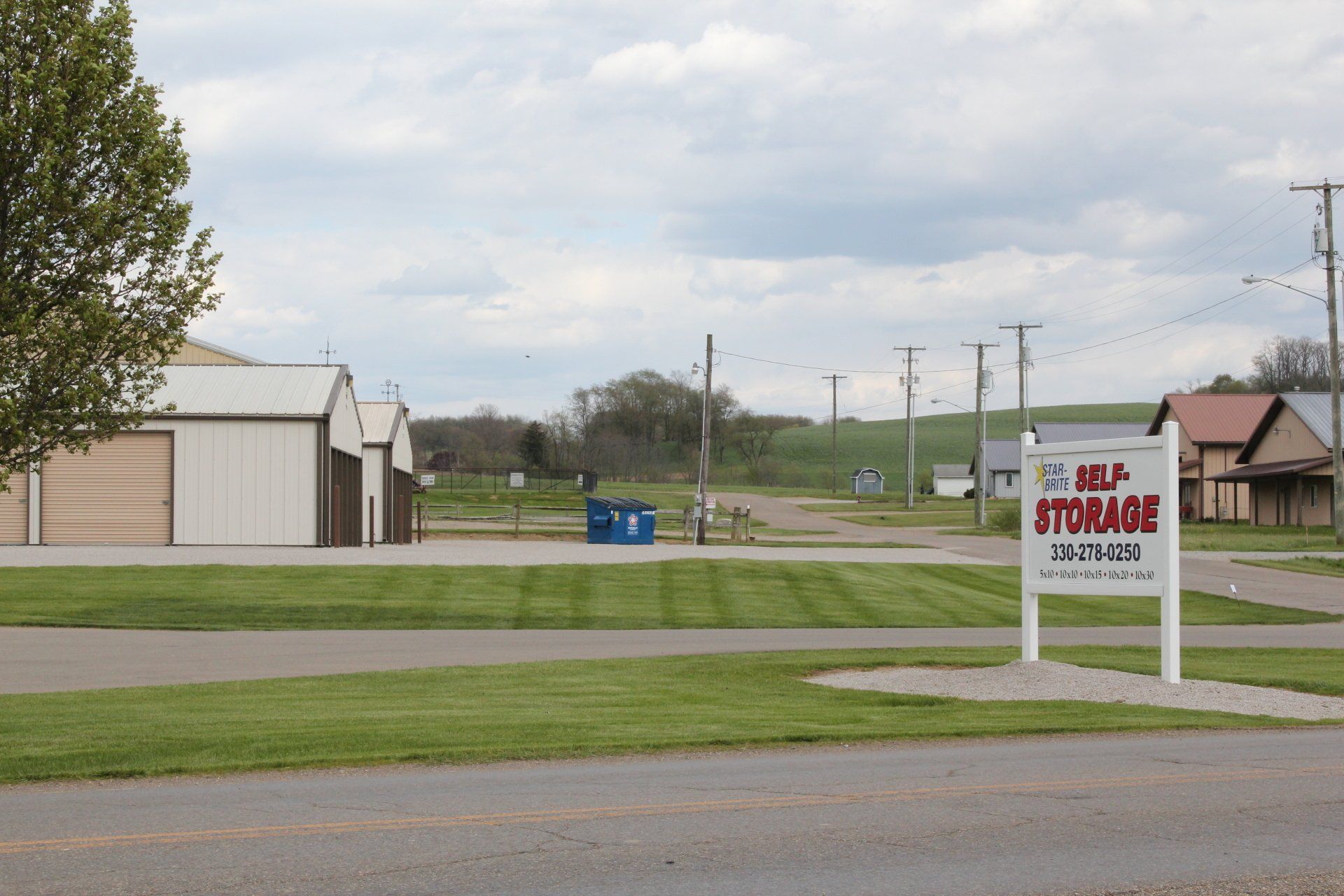 Self-storage facility with a sign on a grassy area, buildings, and overcast sky.