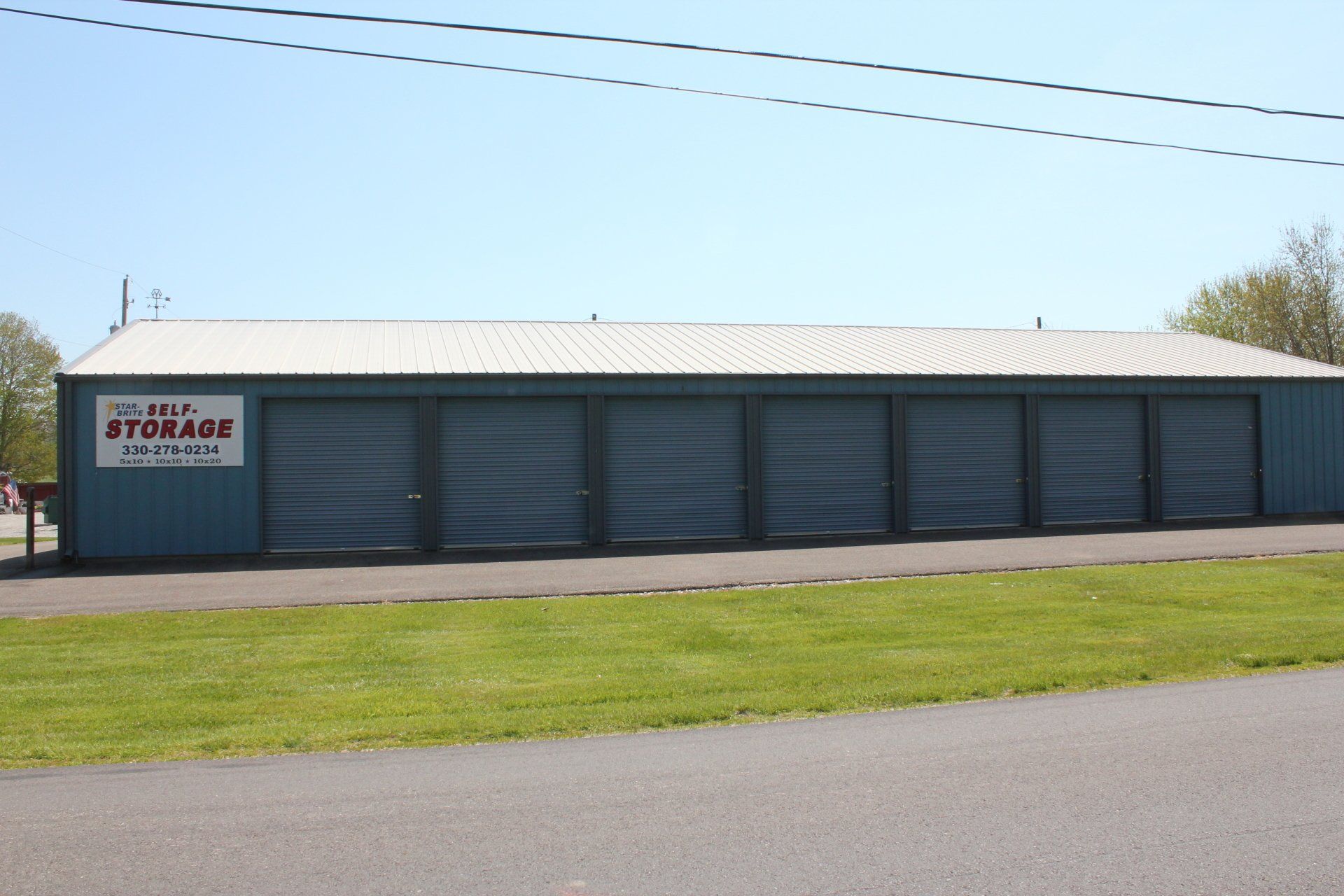 Blue self-storage facility with six units, a white sign, and a green lawn.