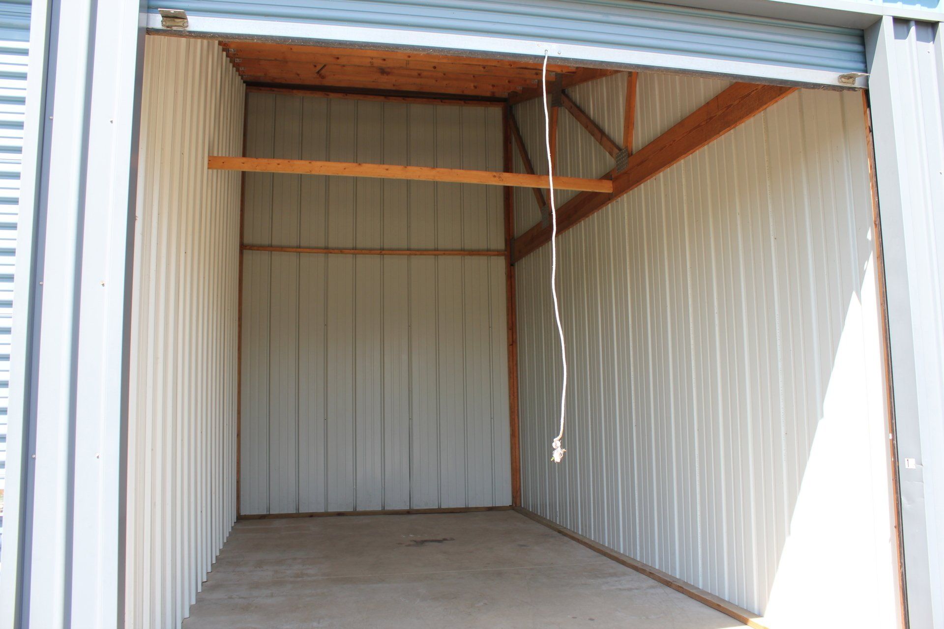 Empty storage unit with gray metal walls and concrete floor; wooden beams are visible.