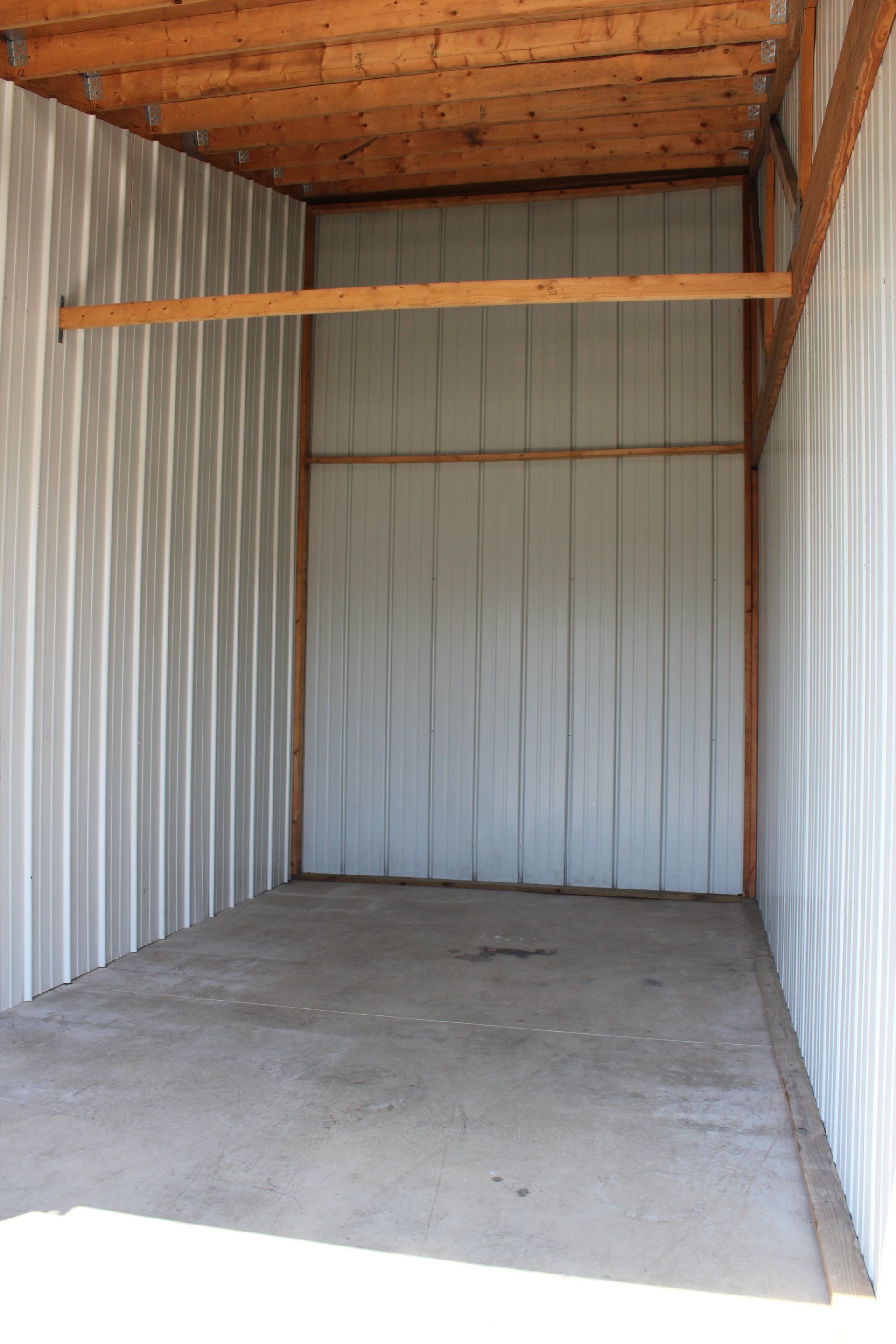 Empty storage unit with gray corrugated metal walls and concrete floor. Wooden beams support the ceiling.
