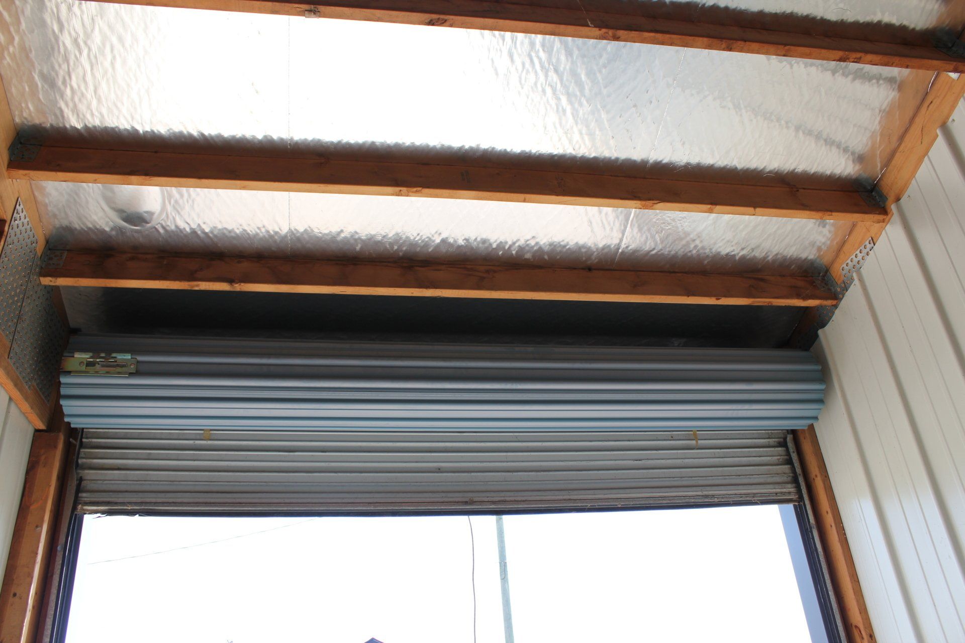Roller shutter above a doorway, with wood beams and silver insulation visible.