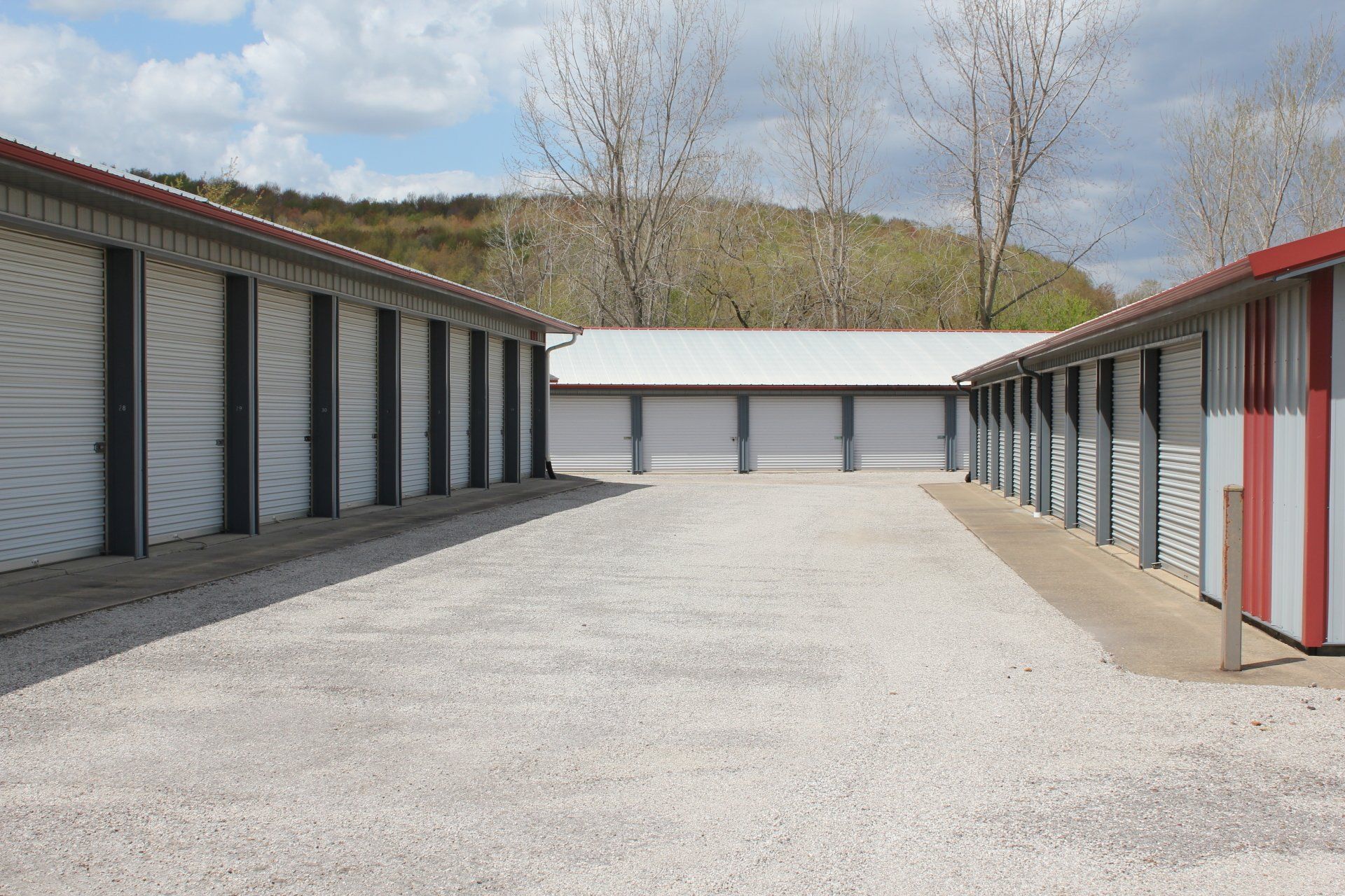 Storage units with white doors and red roofs, gravel lot, outdoors.