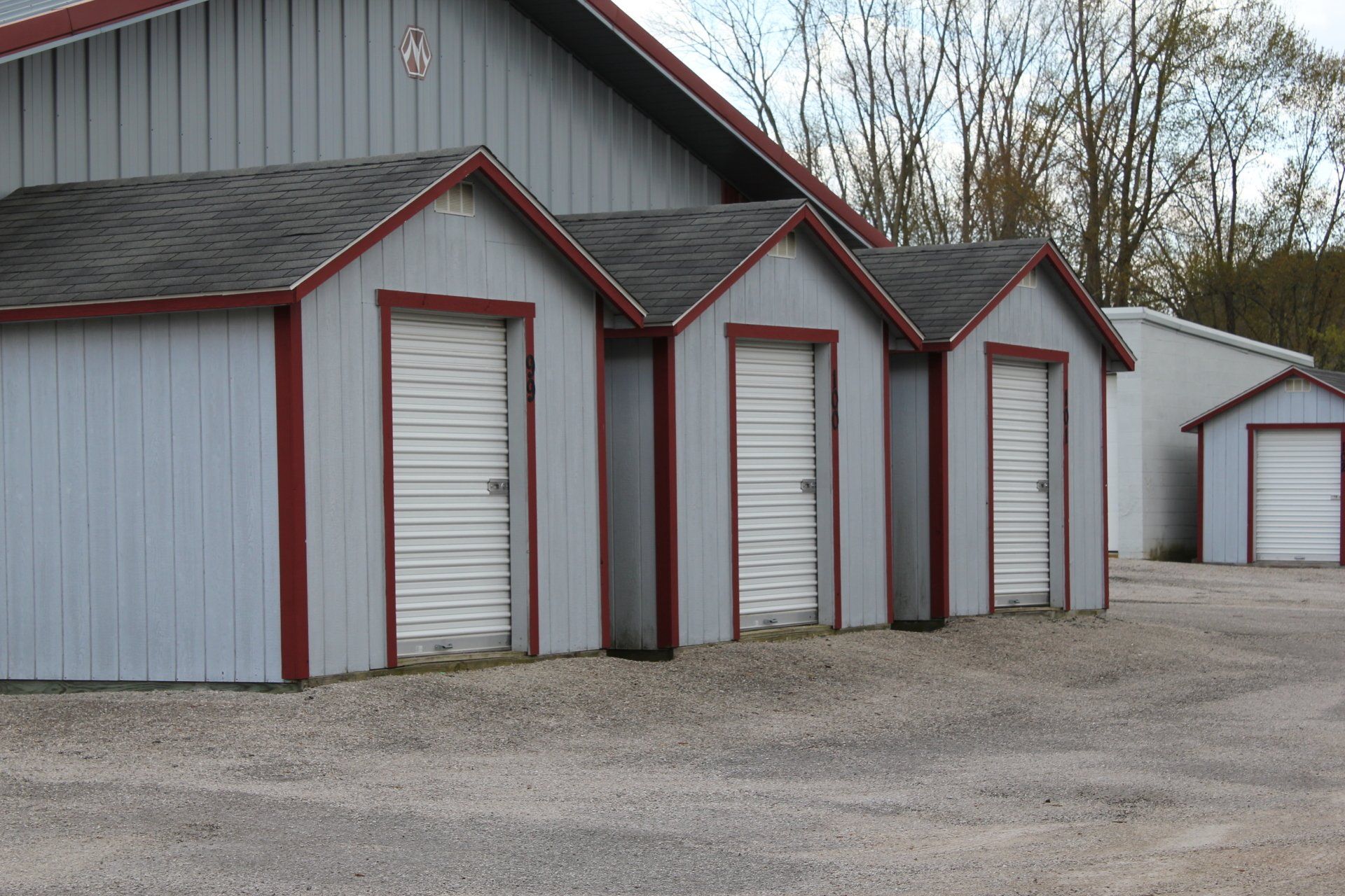 Row of light blue storage units with red trim, gravel lot.