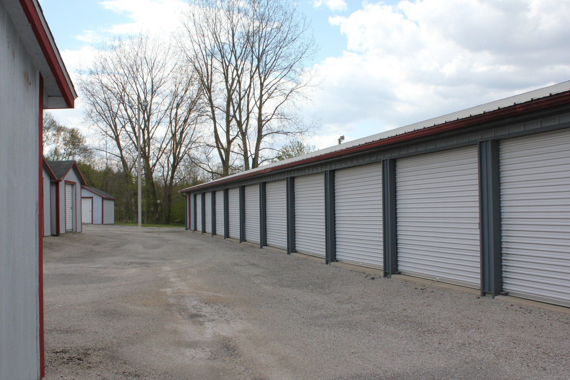 Rows of storage units with gray doors and a gravel driveway.