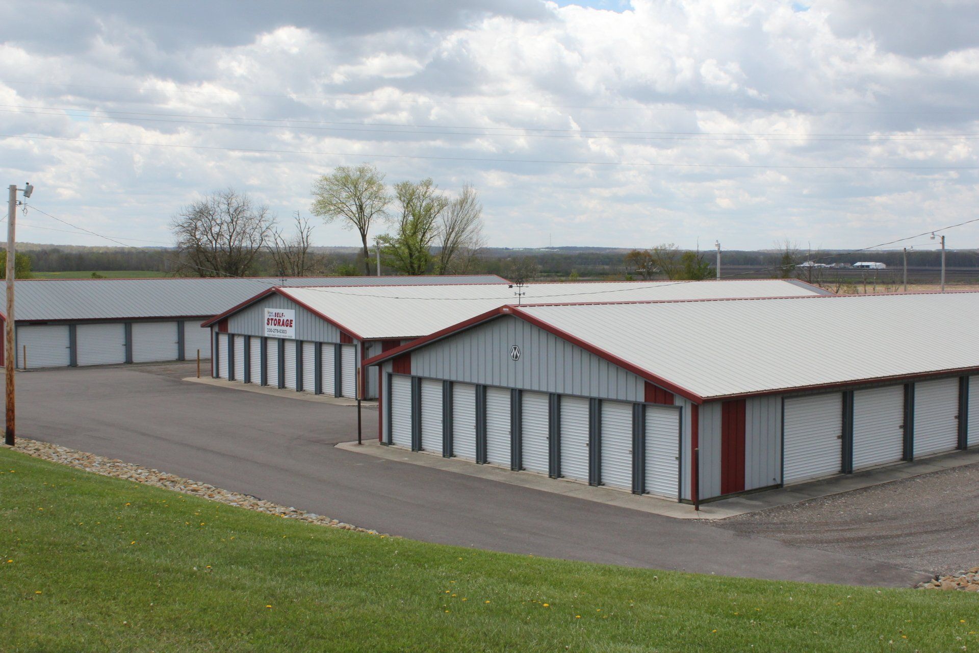 Storage units with gray doors and red trim under a cloudy sky.