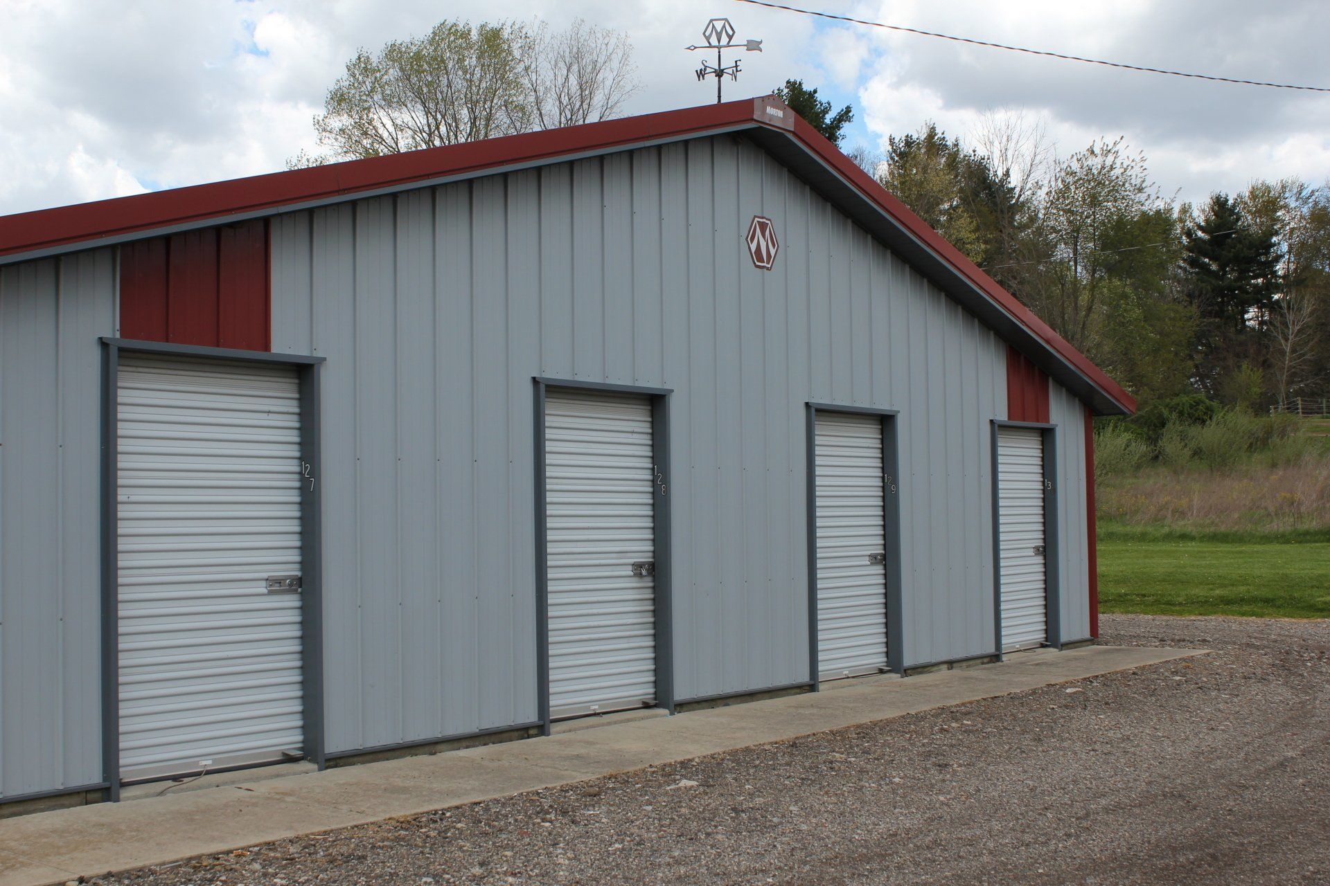 Gray metal storage units with red trim, doors, and a gravel driveway.