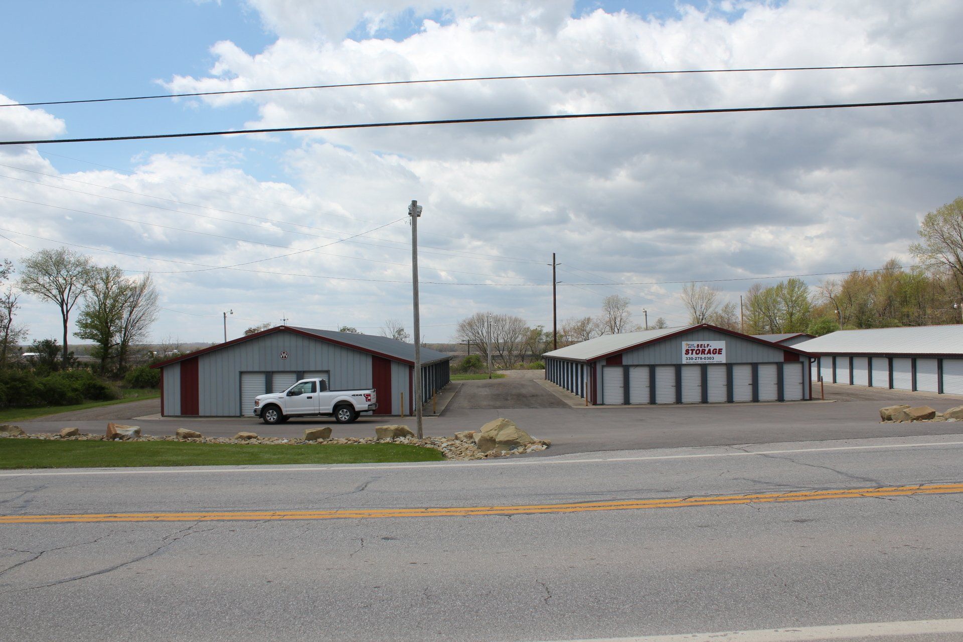 Storage units with a red and gray building and white truck parked in front.