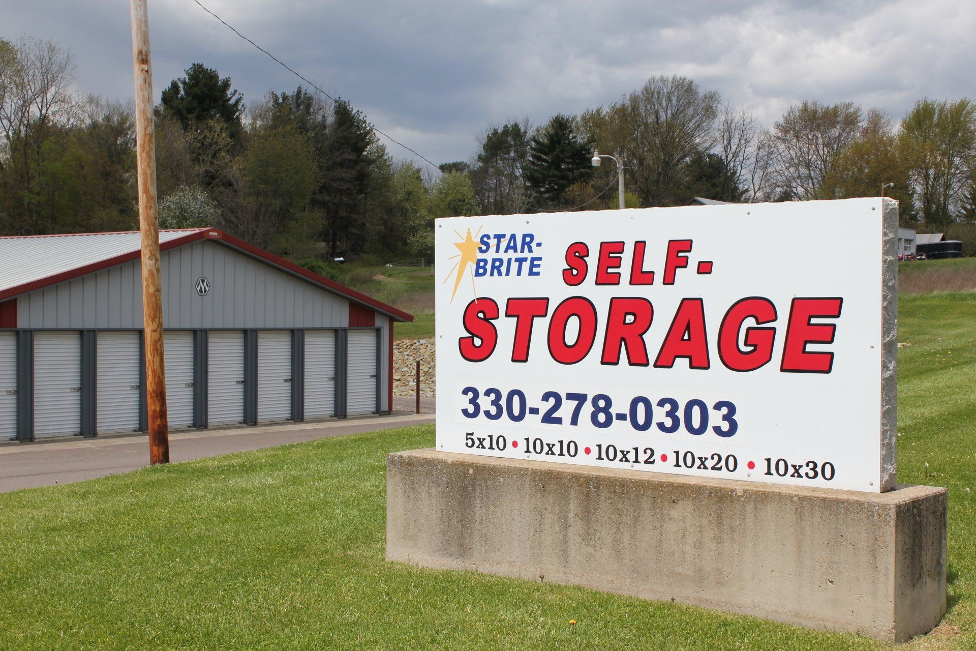 Sign for Star-Brite Self-Storage with phone number and unit sizes. Gray storage units in background.