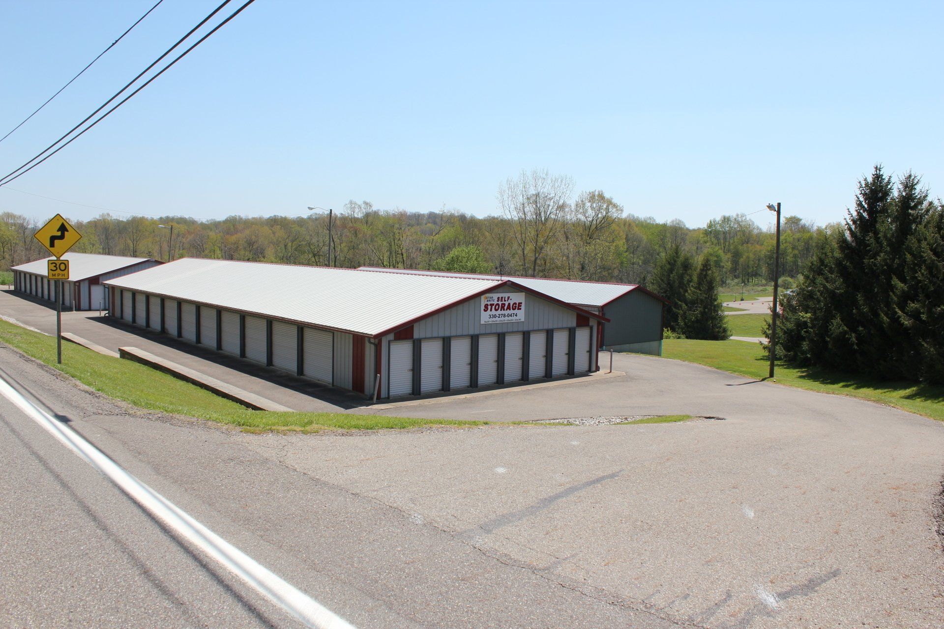 Storage facility with multiple units, gray and red buildings, surrounded by greenery.