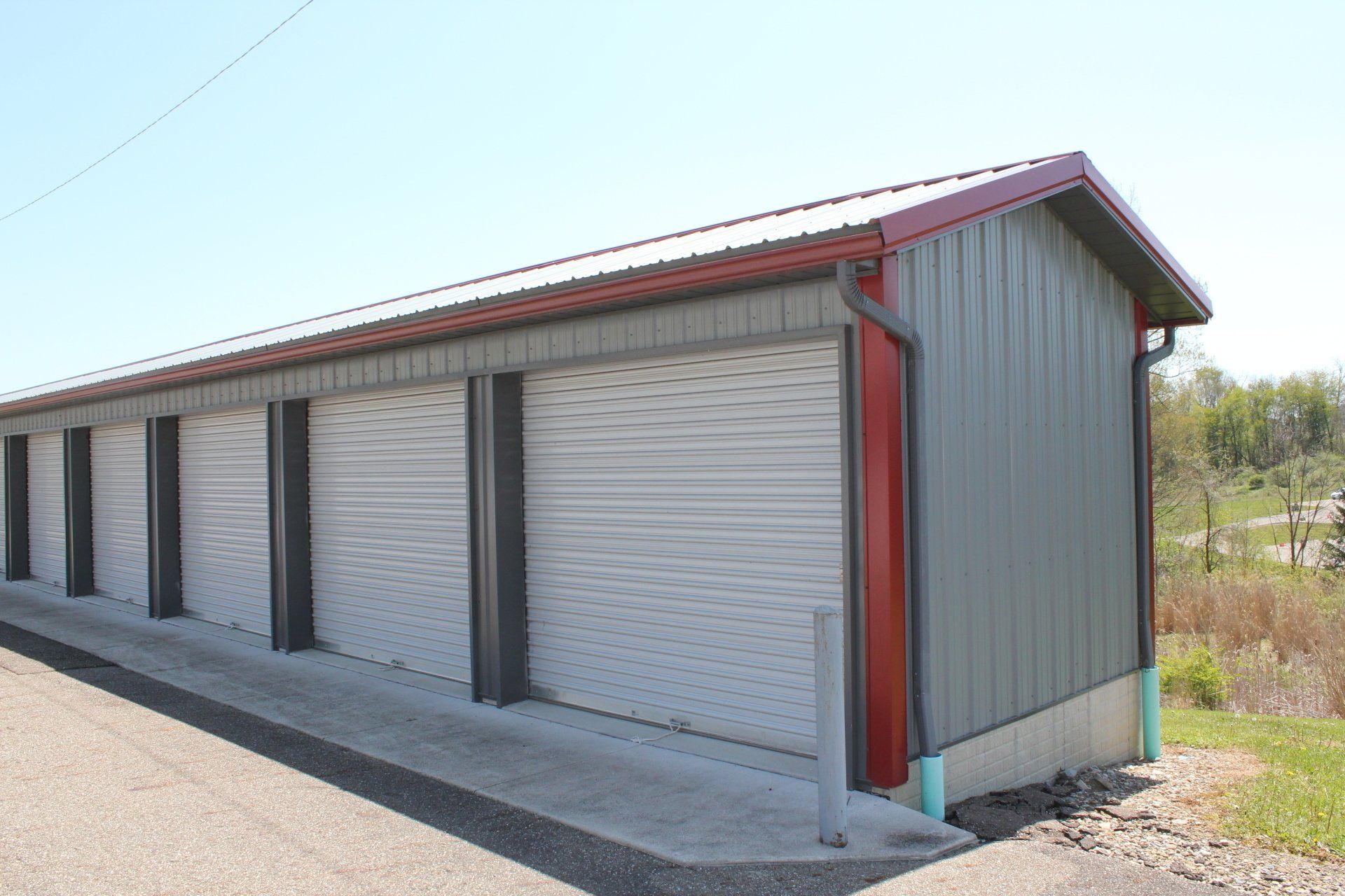 Storage units with gray metal siding and white roll-up doors, red trim, and a gray concrete walkway.