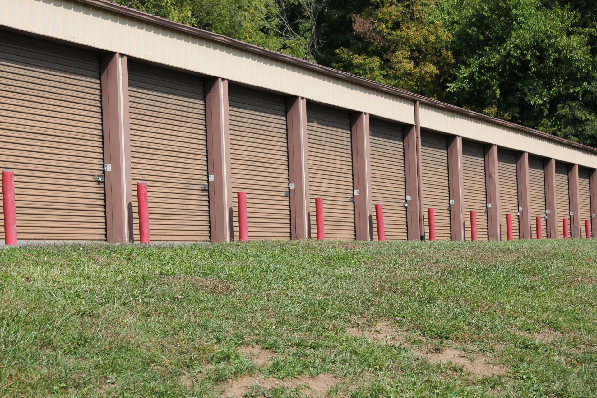 Storage units in a row; brown doors, red posts, green grass, and trees.