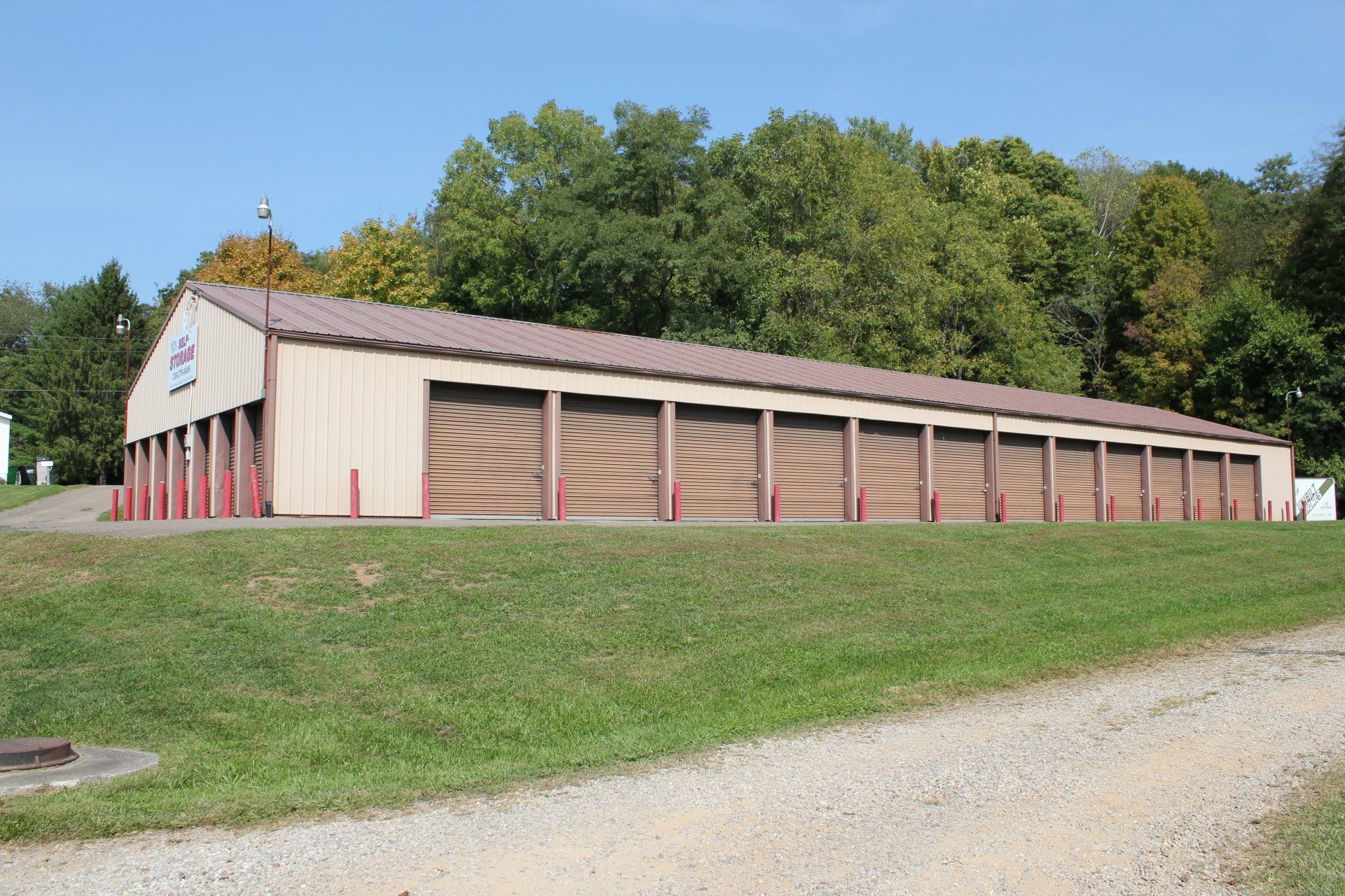 Tan storage units with brown doors, a sloped roof, and a gravel driveway in front.