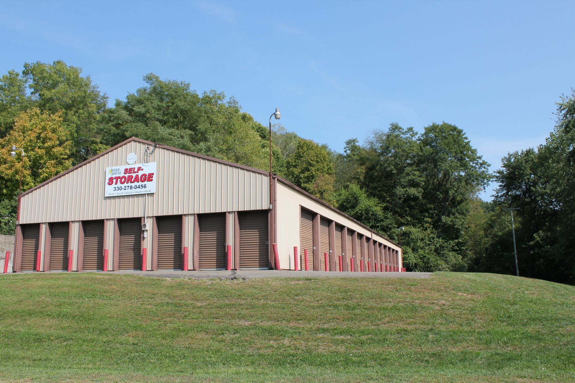 Self-storage facility with brown storage unit doors on a grassy hill, surrounded by trees.