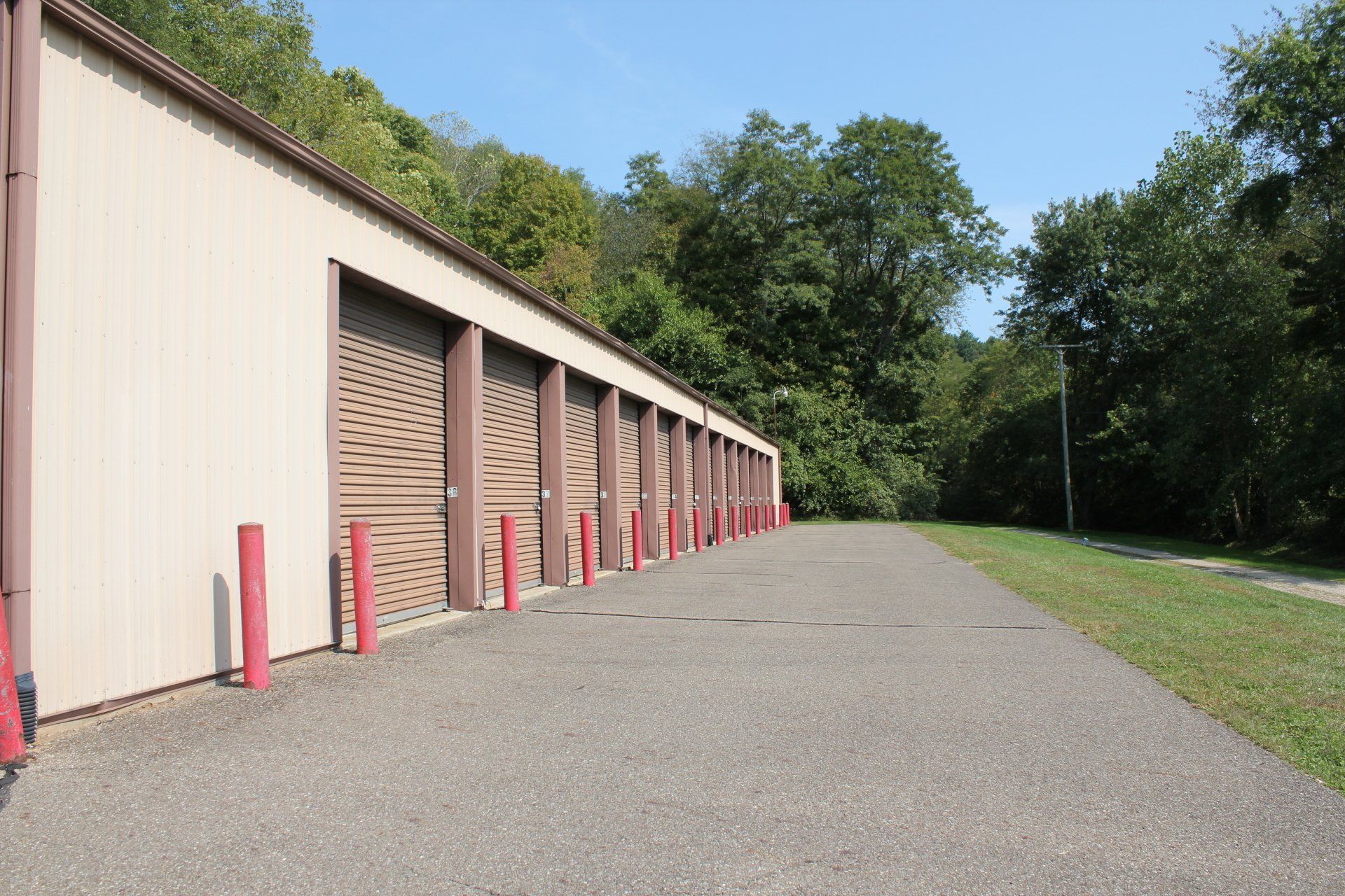 Storage units with brown doors, beige walls, and a paved walkway, in a wooded area.
