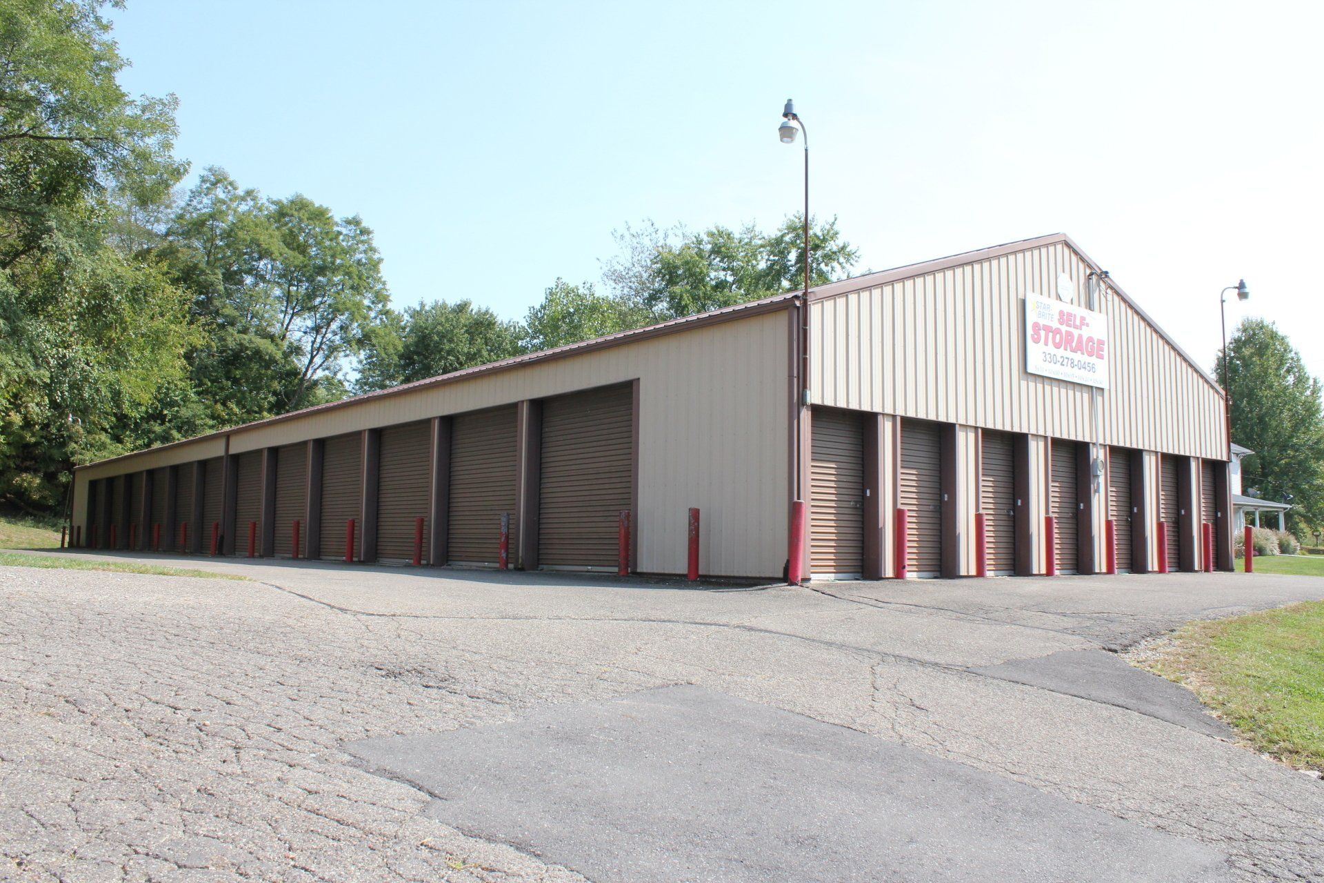 Storage units in a tan metal building with brown doors and red posts, on a gravel lot.