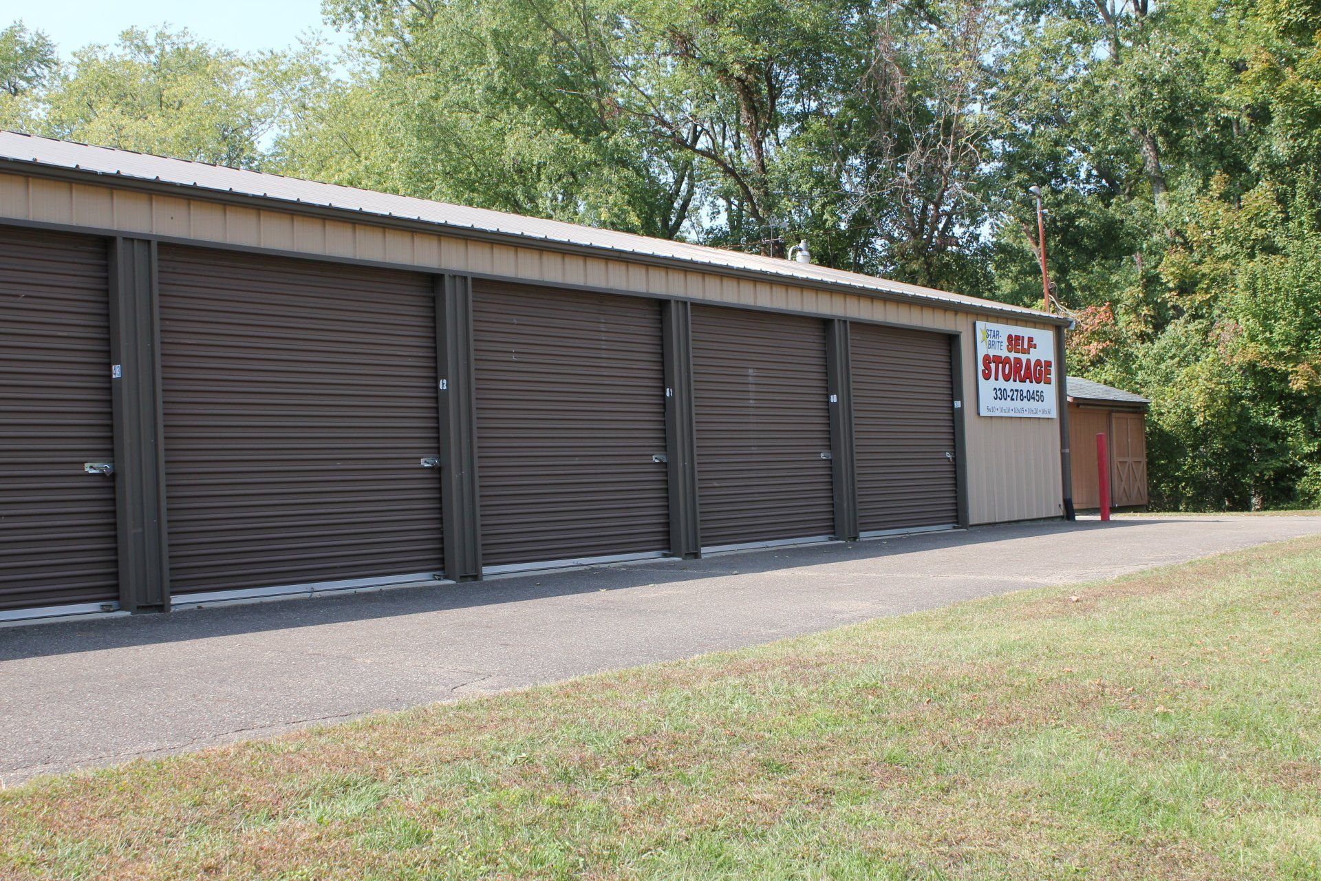 Storage units with brown doors under a tan roof, gravel path, sign for 