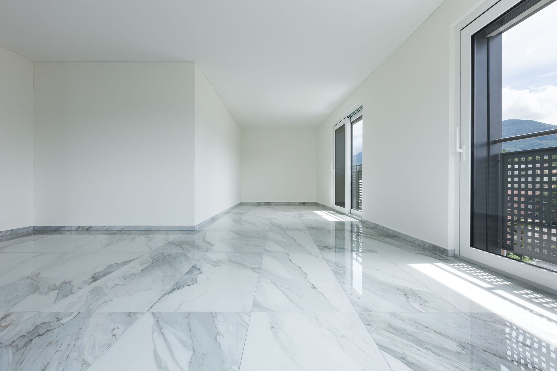A large empty room with a marble floor and a balcony.