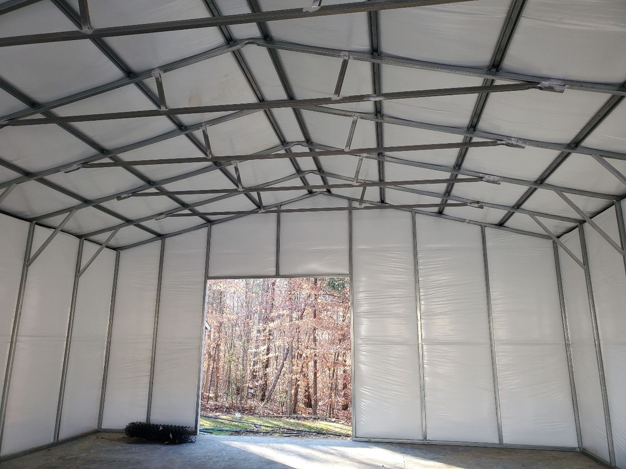Interior view of a white fabric-walled structure with a steel frame, an open doorway, and a view of trees.
