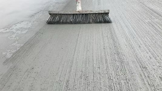 Broom brushing wet concrete, creating a textured, gray surface.