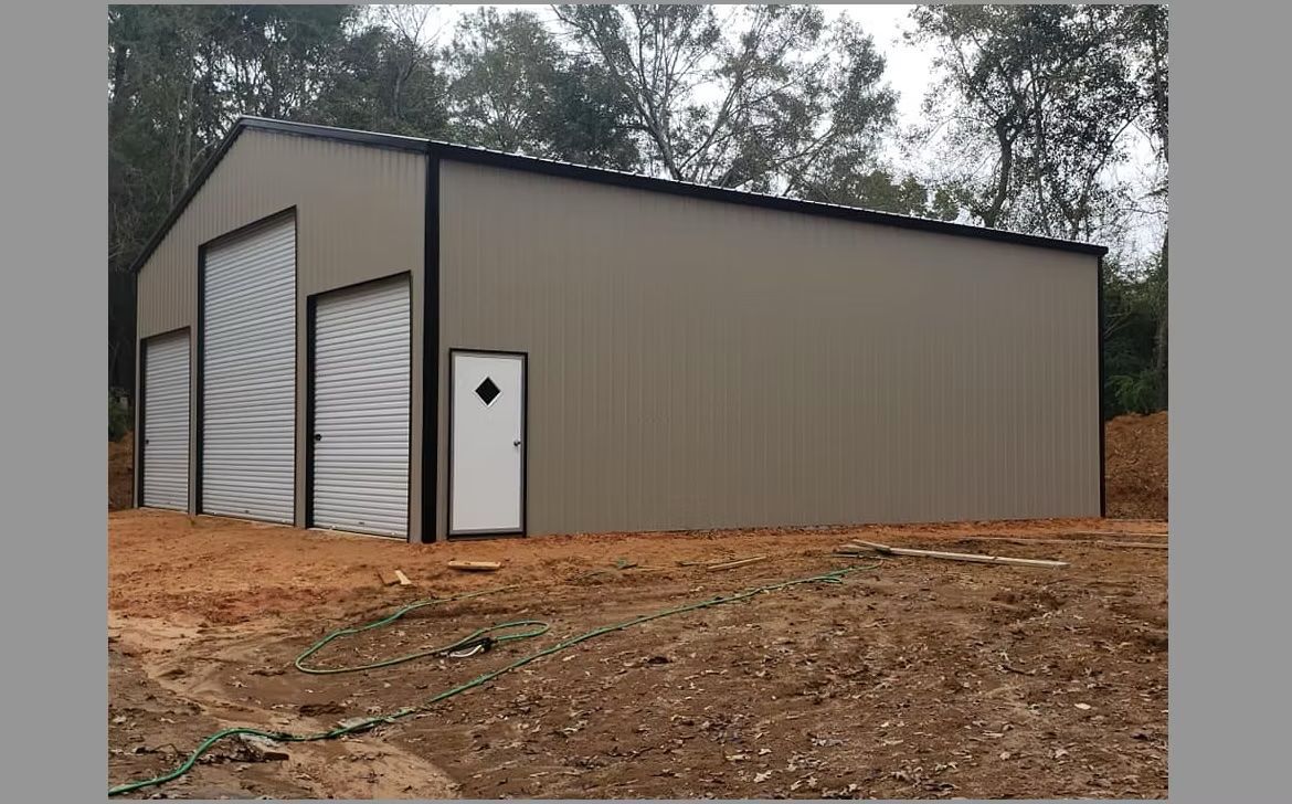 Tan metal building with three garage doors and a white door, set in a dirt lot.