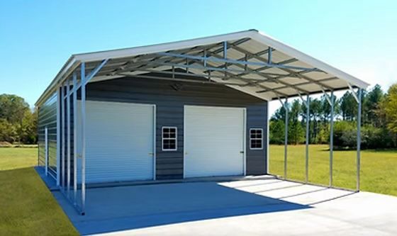 Gray metal garage with white doors, carport attached, blue sky.