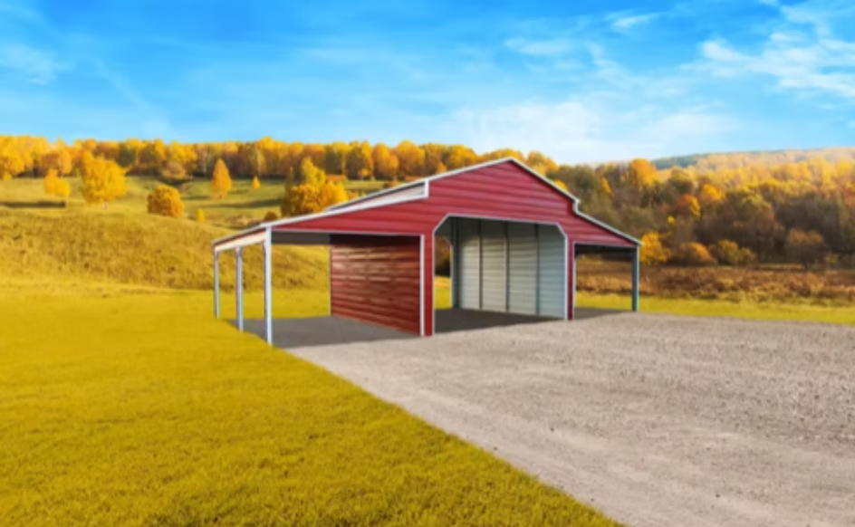 Red and white metal barn with a gravel driveway set in a field with fall foliage.
