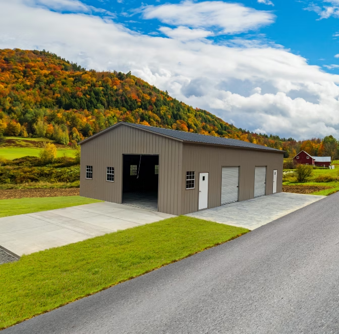 A brown metal building with garage doors, concrete driveway, and a mountain backdrop.