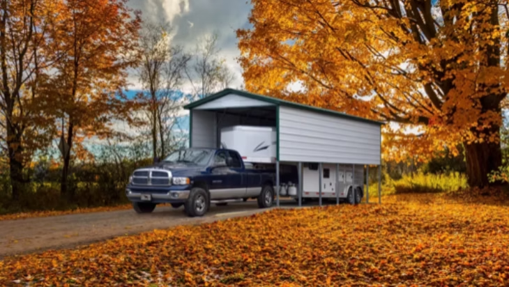 A blue pickup truck with a trailer under a white and green carport in fall.