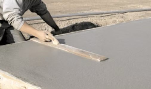 Person smoothing wet concrete with a long wooden float outdoors.