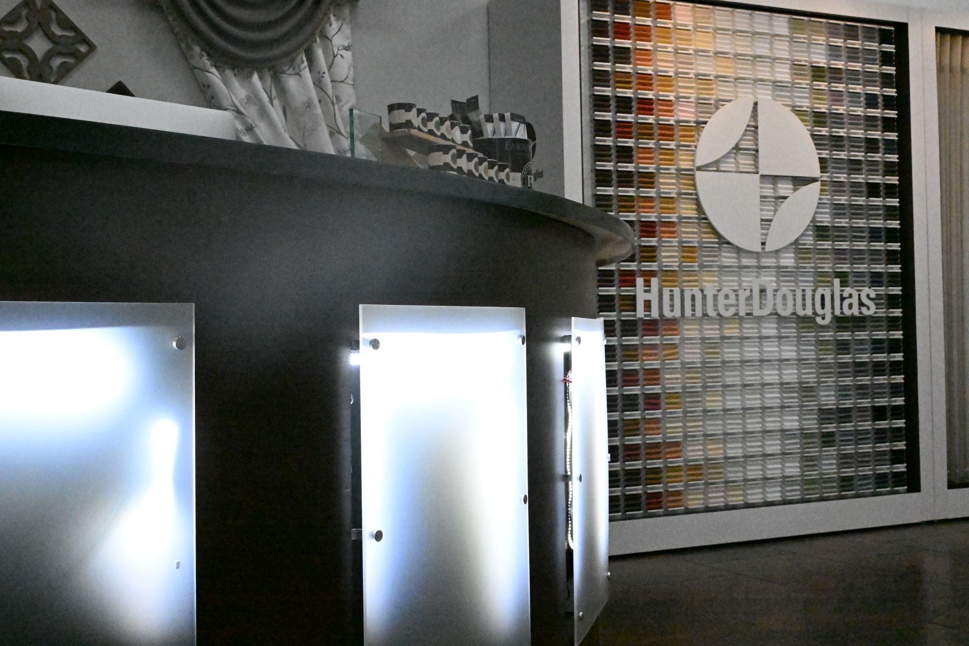 A dark, curved reception desk with backlit frosted panels sits in front of a wall branded with the Hunter Douglas logo.