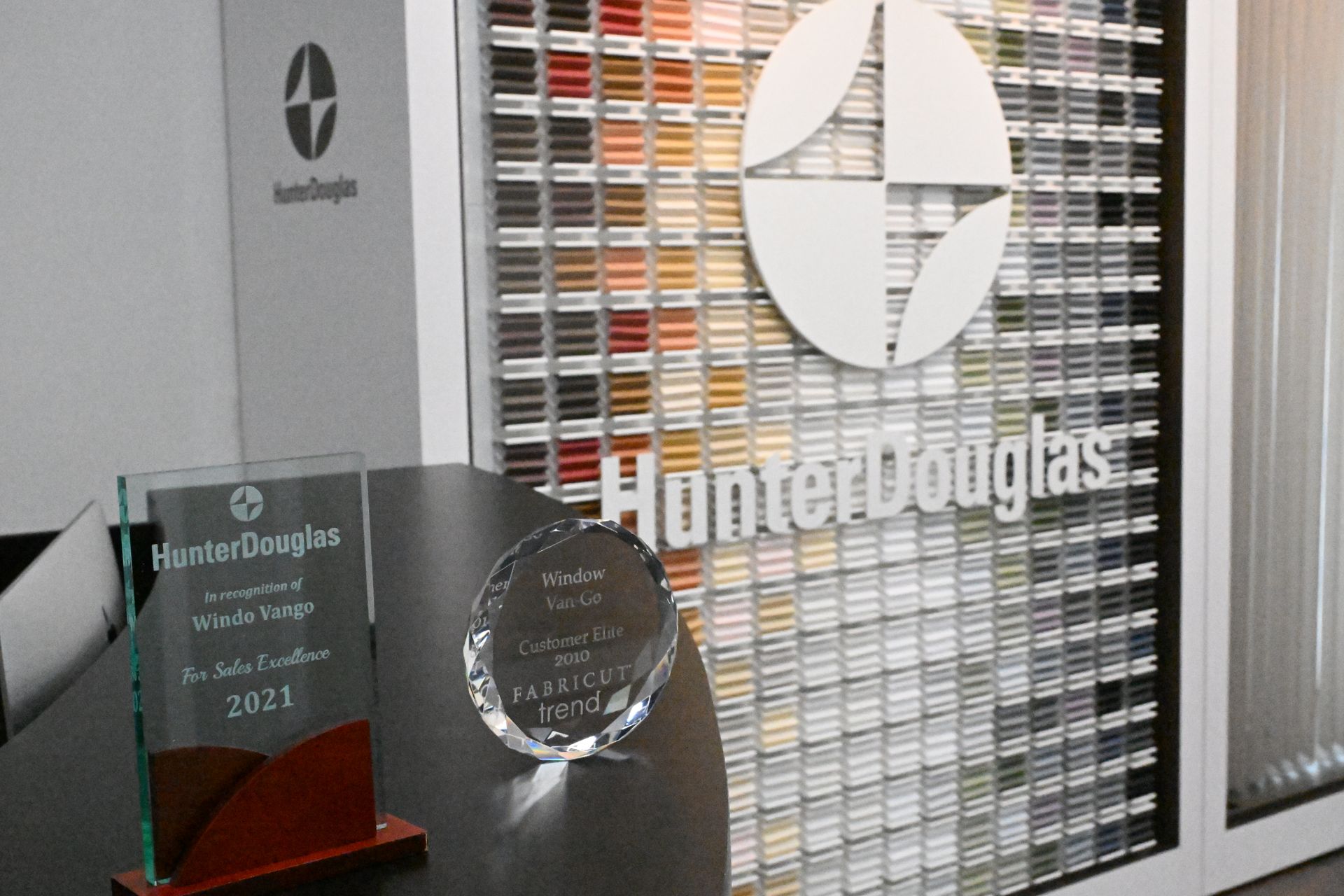 Hunter Douglas logo displayed on a fabric sample wall with two awards on a desk in the foreground.