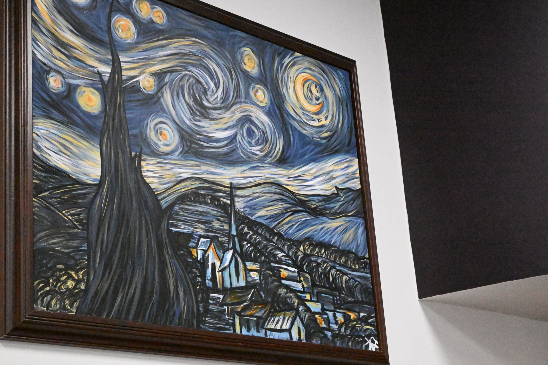 A framed print of Van Gogh’s Starry Night hangs on a white wall next to a dark corner.