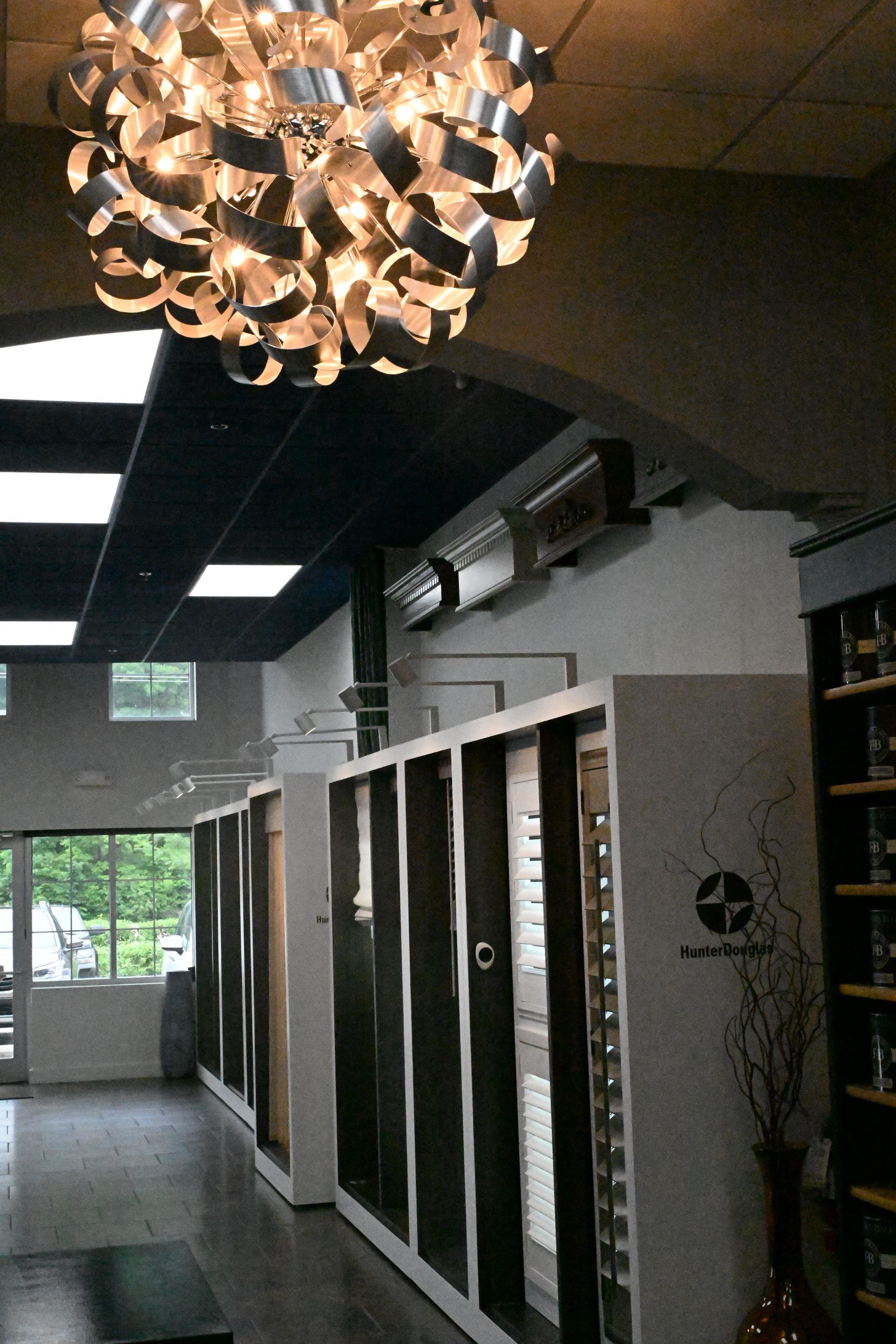 Interior view of a modern showroom featuring a large spiky chandelier above rows of display cabinets and glass windows.