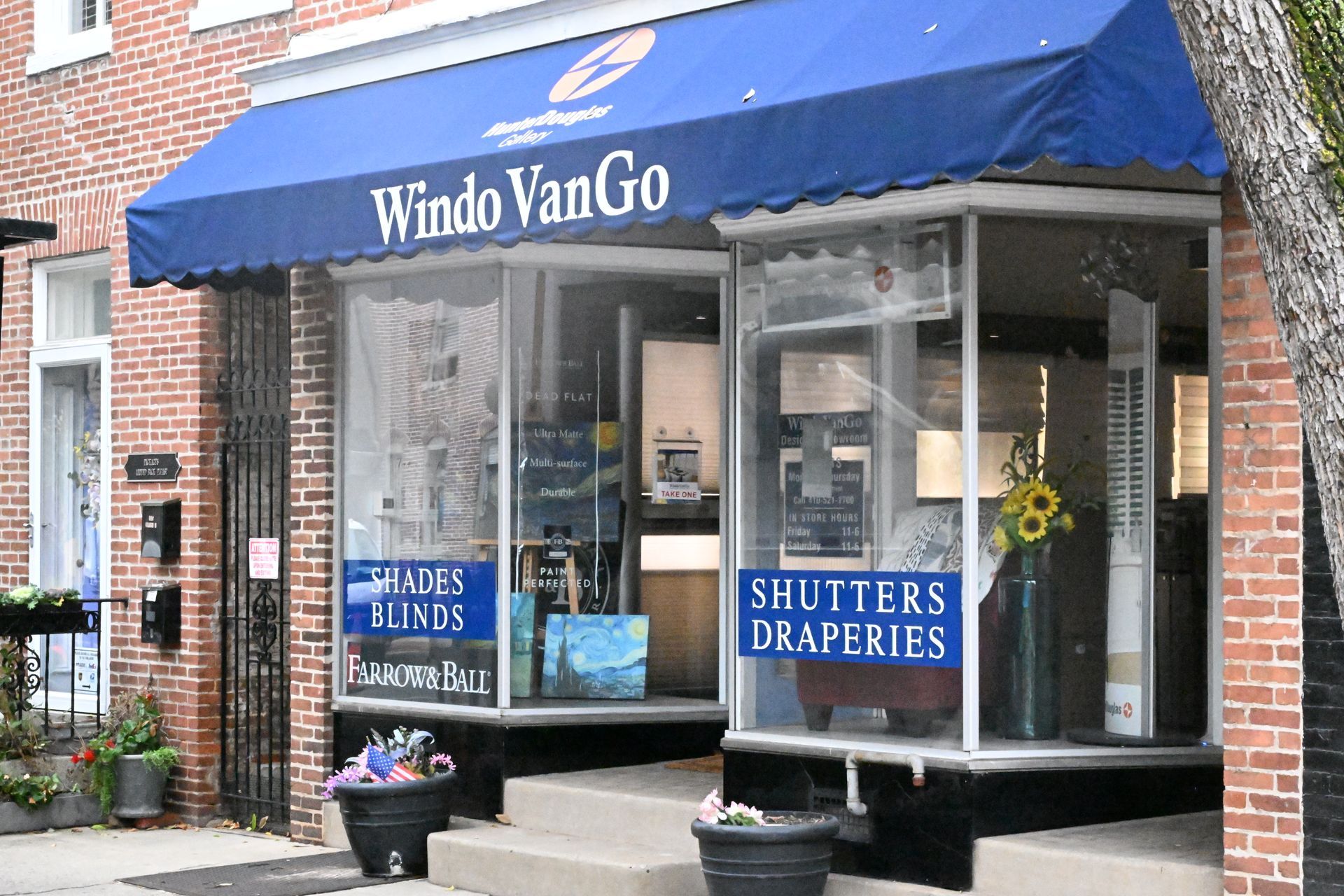 Storefront of Windo VanGo with a blue awning, brick exterior, and window signage for shades, blinds, shutters, and drapes.