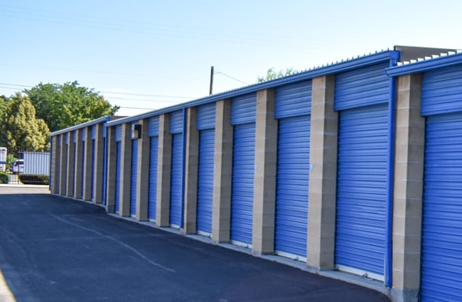 Row of blue storage unit doors with concrete pillars, sunny outdoor setting.