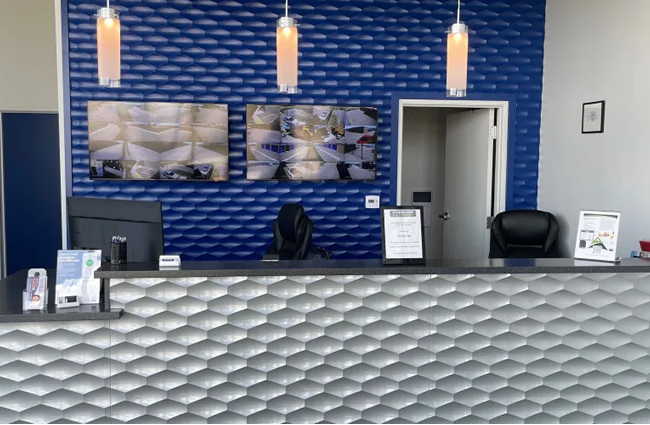 Reception desk in a building with textured blue wall and silver-gray front. Three pendant lights and screens above.