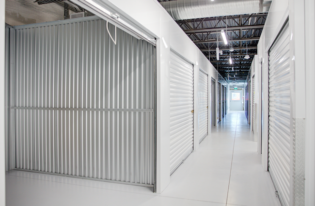 Interior of a storage facility hallway with white units and a metal door.