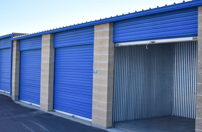 Blue storage units, one open, along a paved walkway. Concrete pillars frame each unit.